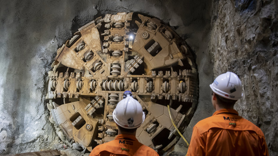 An on the ground view of two Sydney Metro construction workers looking at Tunnel Boring Machine(TBM) Kathleen breakthrough at Blues Point. 