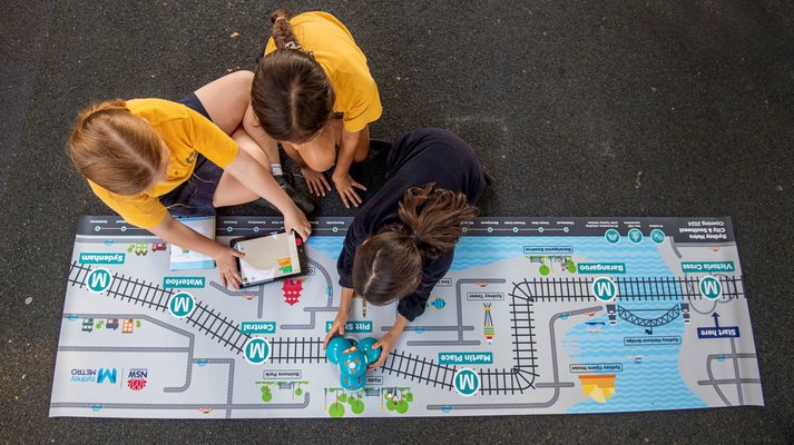 Three students from Petersham Public School holding the tablet and the dash robot that is sitting on top of an alignment map