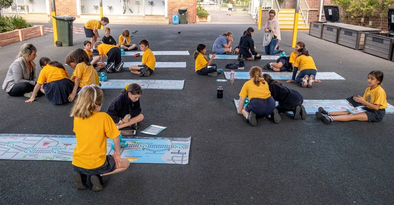 A group of 19 students and one teacher from Petersham Public School using the dash robost that are sitting on top of an alignment map