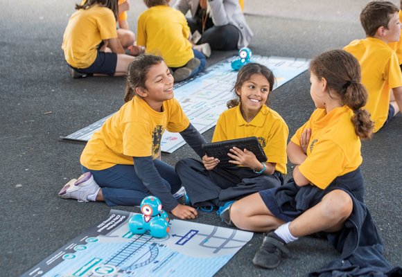 Three students from Petersham Public School smiling behind the dash robot that is sitting on top of an alignment map