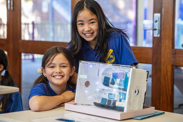 Two girls in school uniforms smiling behind a project they created.