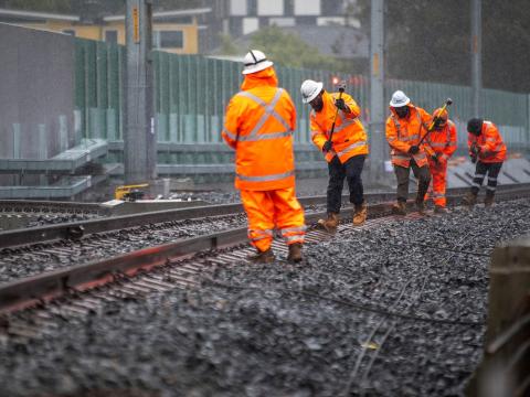 5 construction workers in high viz, using a tool to realign the train track.