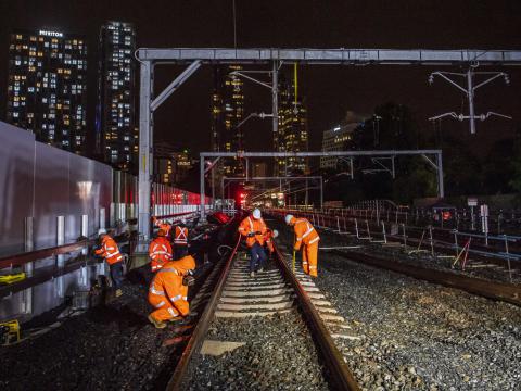Tracks are being reconnected by construction workers at night between Artarmon and Chatswood stations. Sydney city skyline can be seen in the background.