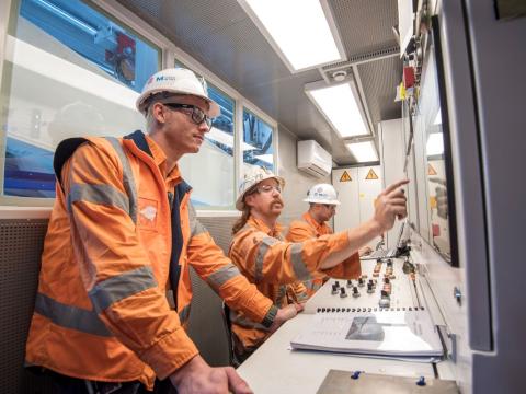 Three Sydney Metro workers in safety gear looking at the screens