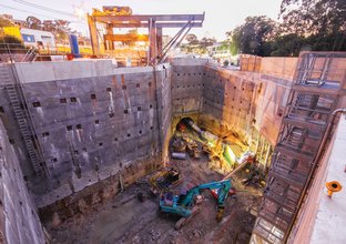 A bird's eye view from the ground looking down into the construction site showing four excavators digging and machines entering the tunnel at Sydney Metro's Epping Services facility. 