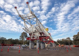 An on the ground view looking up showing the metal structure of the first span of Sydney Metro's skytrain with a Gantry crane lifting the structure in place.