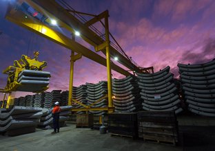 Several piles of concrete segments are stacked in a row while a construction worker looks on at a purple sky at dusk.