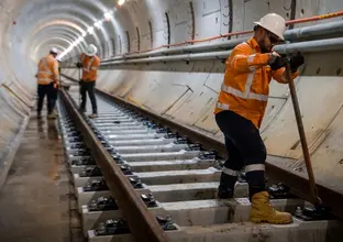 Three construction workers in high viz and hard hats are working on the installation of the track in the tunnel under Sydney Harbour.