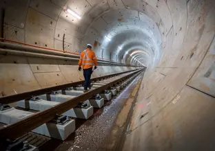 Construction worker with back to photo is walking along the track inside the tunnel