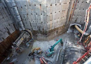 A bird's eye view from the ground looking down into the construction site showing two excavators digging and construction workers by the two tunnels at Sydney Metro's Epping Services facility. 