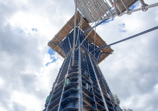 A ground up view of the skytrain pier during construction and wrapped in scaffolding on a cloudy day.