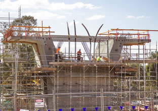 Four construction workers on the scaffolding surrounding the segment of concrete construction on Sydney Metro's skytrain. 