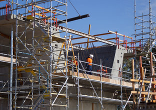 Two construction workers on the scaffolding surrounding the segment of concrete construction on Sydney Metro's skytrain. 