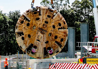 TBM4 Maria cutterhead is being lifted from Epping construction site while construction workers look on.