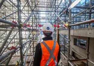 Construction worker with back to photo is standing amongst scaffolding