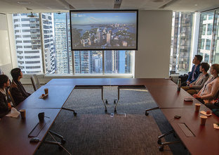 A group of people are sitting around a U-shaped boardroom table looking at a presentation on screen.