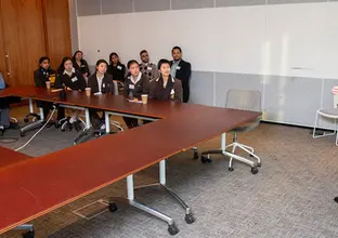 A man is presenting to a several people sitting around an O-shaped table in a board room 