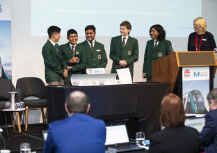 Students present to a panel of judges on stage at the Metro Minds STEAM challenge finals event.