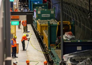An arial view showing four construction workers on the platform as a freight train is delivering materials to the platform at East Coast Rail Link's Macquarie Park Station.