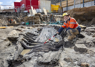 A man in high visibility PPE shows the remains of an old heritage boat found during excavations at Barangaroo Station site.