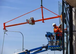 A close up shot of two construction workers installing glass windows from a cherry picker at Sydney Metro's Kellyville Station. 