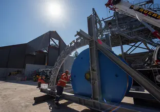 A construction worker pushes a large spool that's sitting on a steel structure at a construction site.