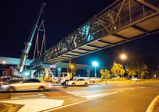An on the ground view showing the final segment of the pedestrian walkway that has been crane lifted into place  at night at Sydney Metro's Kellyville Station.