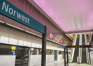 The bottom of the escalators at Norwest Station platform. A blue Norwest sign is in focus with platform screen doors in the background.