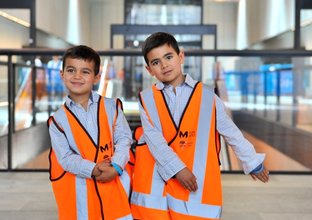 Two young boys are posing for the camera in orange high vis construction vests at Norwest Station.