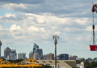 An ariel view looking across at a crane lifting track material into place between Sydney Metro's Sydenham to Bankstown Stations with the Sydney skyline in the background. 