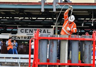 A close up shot of a construction worker spraying pipes in the station box at Sydney Metro's Central Station. 