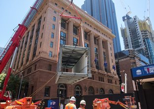 An on the ground view looking up at the pedestrian walkway being craned into place at the construction site of Sydney Metro's Martin Place Station. 