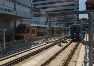 An on the ground view looking across the station platform as a Sydney Metro Train arrives at the platform next to a Sydney Trains train at Chatswood Station. 