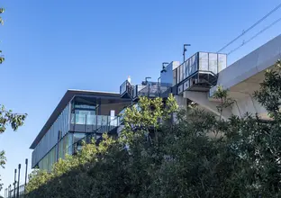 An on the ground view looking up to see behind the trees the completed Sydney Metro's Kellyville Station. 