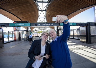 An older couple are taking a selfie outside Castle Hill Station escalators.