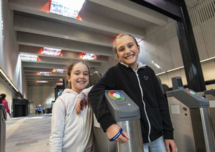 Two young girls pose outside the opal card readers at the entrance of Castle Hill Station.