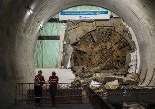 The cutterhead of tunnel boring machine Mum Shirl can be seen breaking through the wall at Martin Place Station. Two construction workers in high viz can be seen watching.
