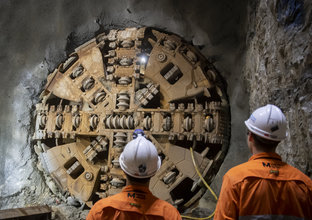 An on the ground view of two Sydney Metro construction workers looking at Tunnel Boring Machine(TBM) Kathleen breakthrough at Blues Point. 