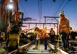 An on the ground view of four construction workers laying the train tracks.