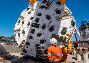 An on the ground view of a construction worker looking up at the cutterhead of a Tunnel Boring Machine (TBM) at Marrickville. 