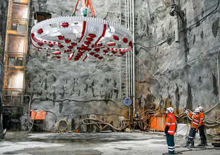 An on the ground view of three construction workers moving into place the overhead Cutterhead Lift of Tunnel Boring Machine (TBM) Mum Shirl  at Sydney Metro's at Barangaroo site. 