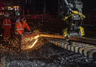 Worker cutting the rail track at night. There is sparks coming off the track and 2 workers in personal protective equipment