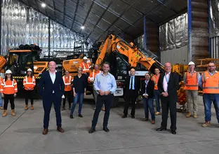 Construction workers and Sydney Metro executives pose for a photo at a construction site with heavy machinery in the background.