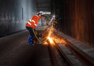 A worker in protective clothing is welding the track at Marrickville Dive site. Sparks can be seen from the welding.