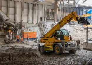 A yellow excavator digs up spoil at the entry to the construction tunnel within the metro box at Central Station.