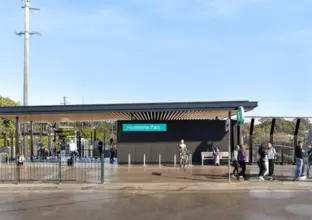 An artists impression of the entry to Hurlstone Park Station. There are people walking around and blue sky in the background.