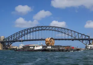 Tunnel Boring Machine (TBM) Kathleen being moved on a barge on the water under Sydney Harbour Bridge. 