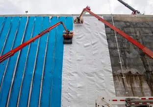 Workers in High Viz are on two Cherry picker lifts installing blue waterproof sheeting to the walls of Waterloo Station box.