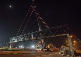 Construction on the Bella Vista pedestrian bridge at night time. The bridge crosses over a large road with many trucks and machinery on site.