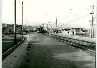 A black and white image of Cooks River Road, Sydnebgam from 1928 showing the road  with old tram tracks to the right of the image and a tram in the background (Image Courtesy of Inner West Council Library and History)